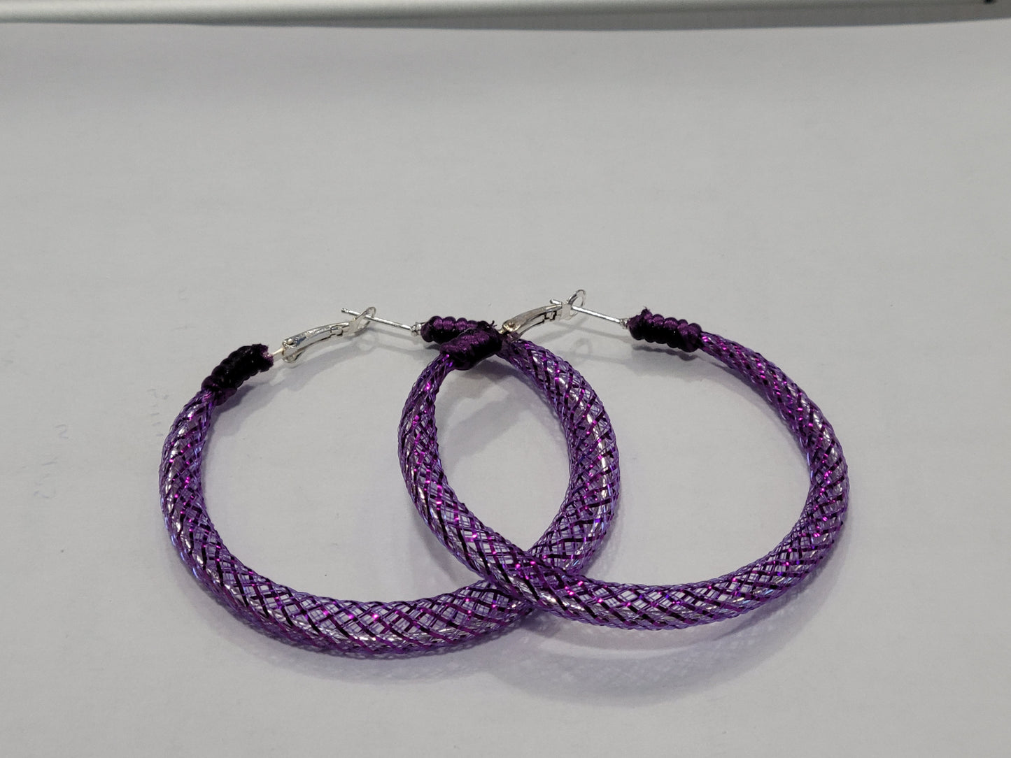 Purple braided lace hoop earrings on a gray background