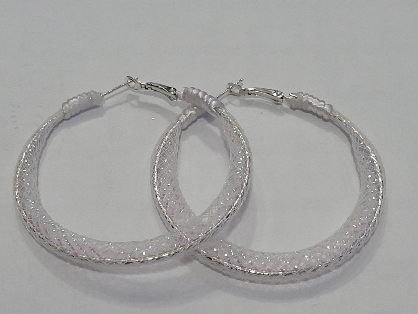Pair of white lace hoop earrings with glittery finish on a gray background