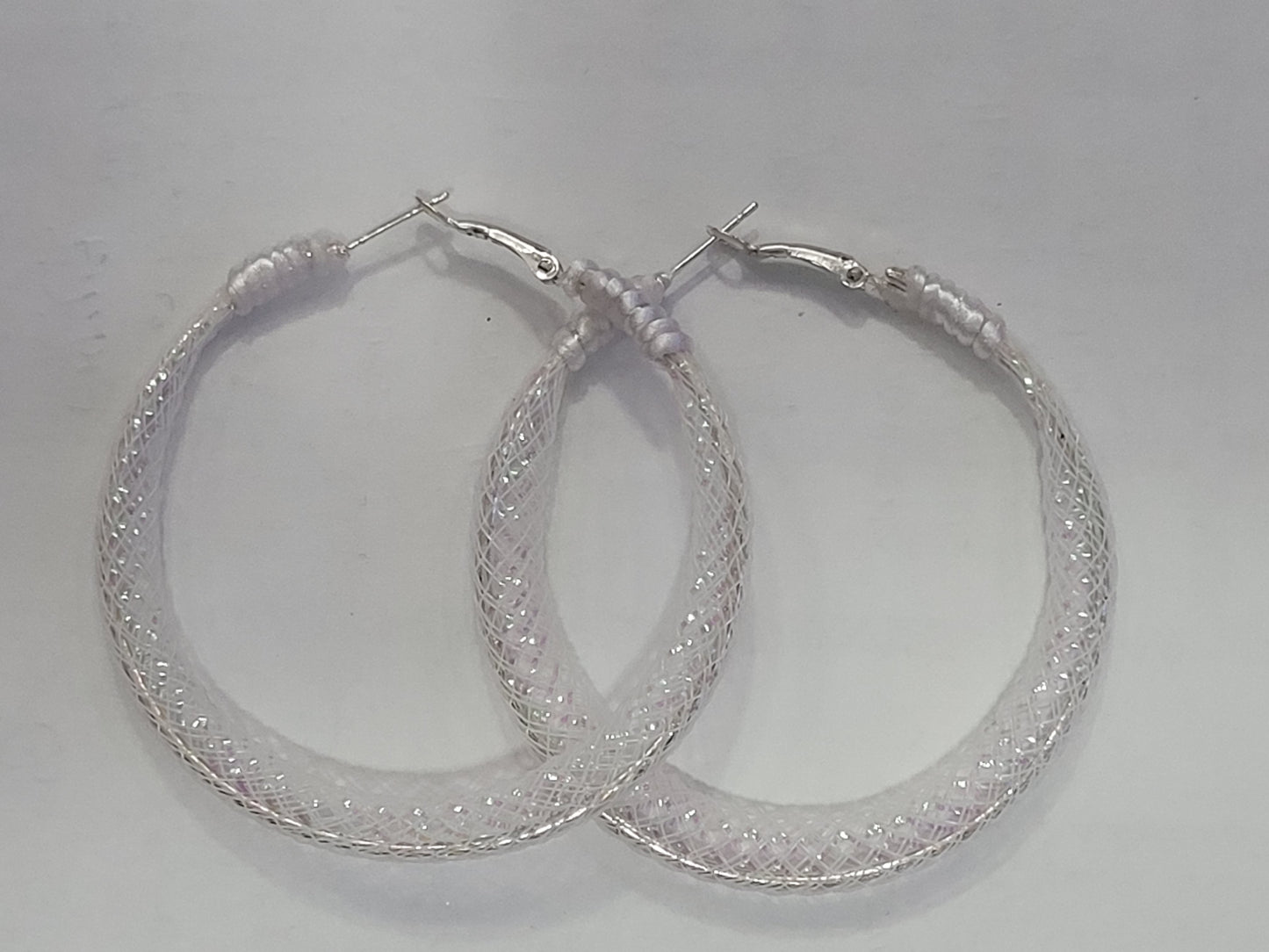 Pair of white lace and silver hoop earrings on a light gray background
