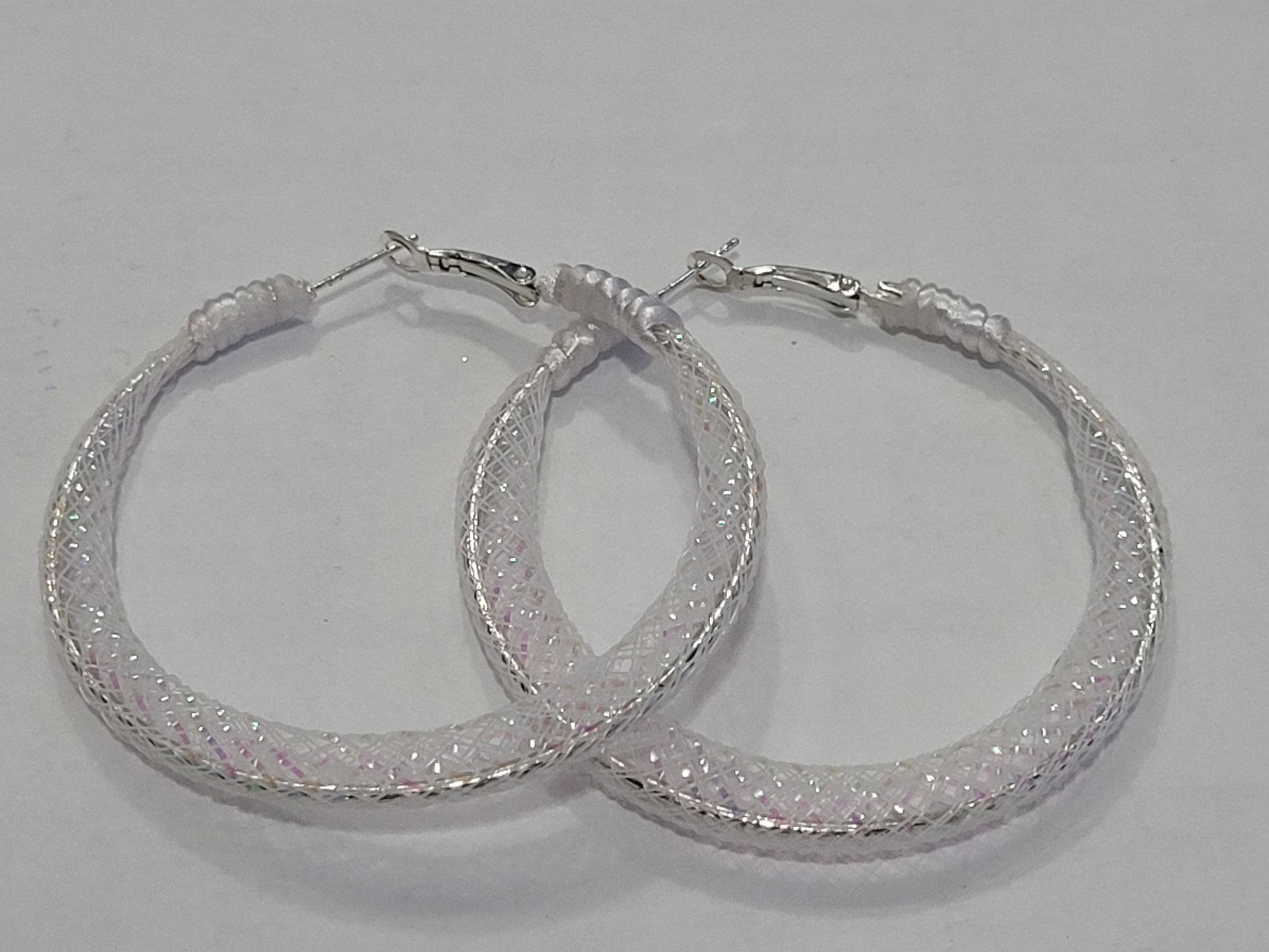 Pair of white lace hoop earrings with glittery finish on a gray background