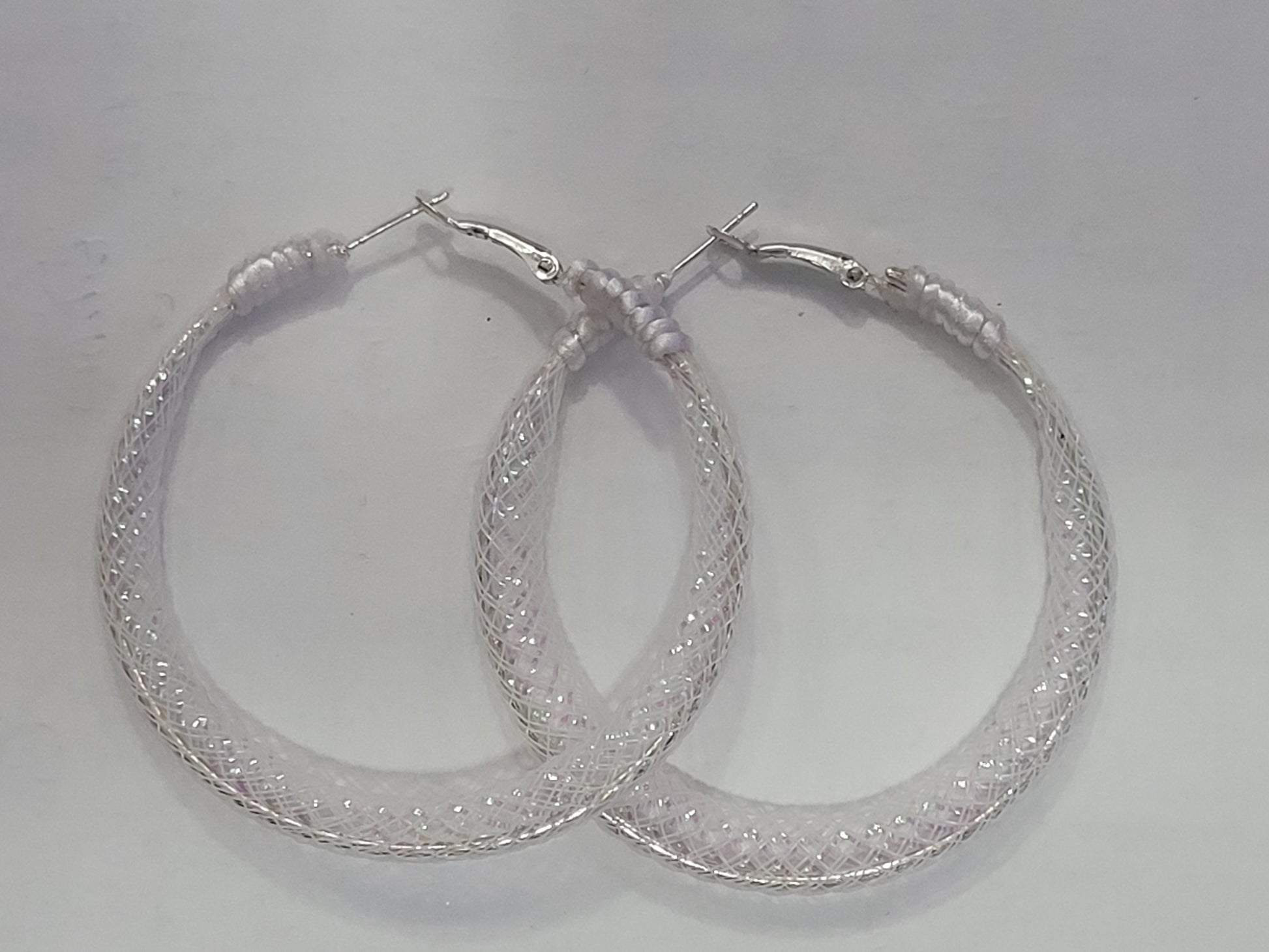 Pair of white lace and silver hoop earrings on a light gray background
